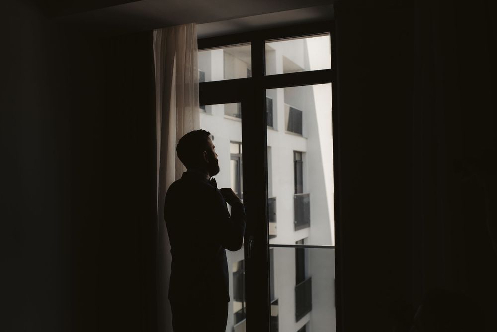Silhouette of person standing by window in formal attire.