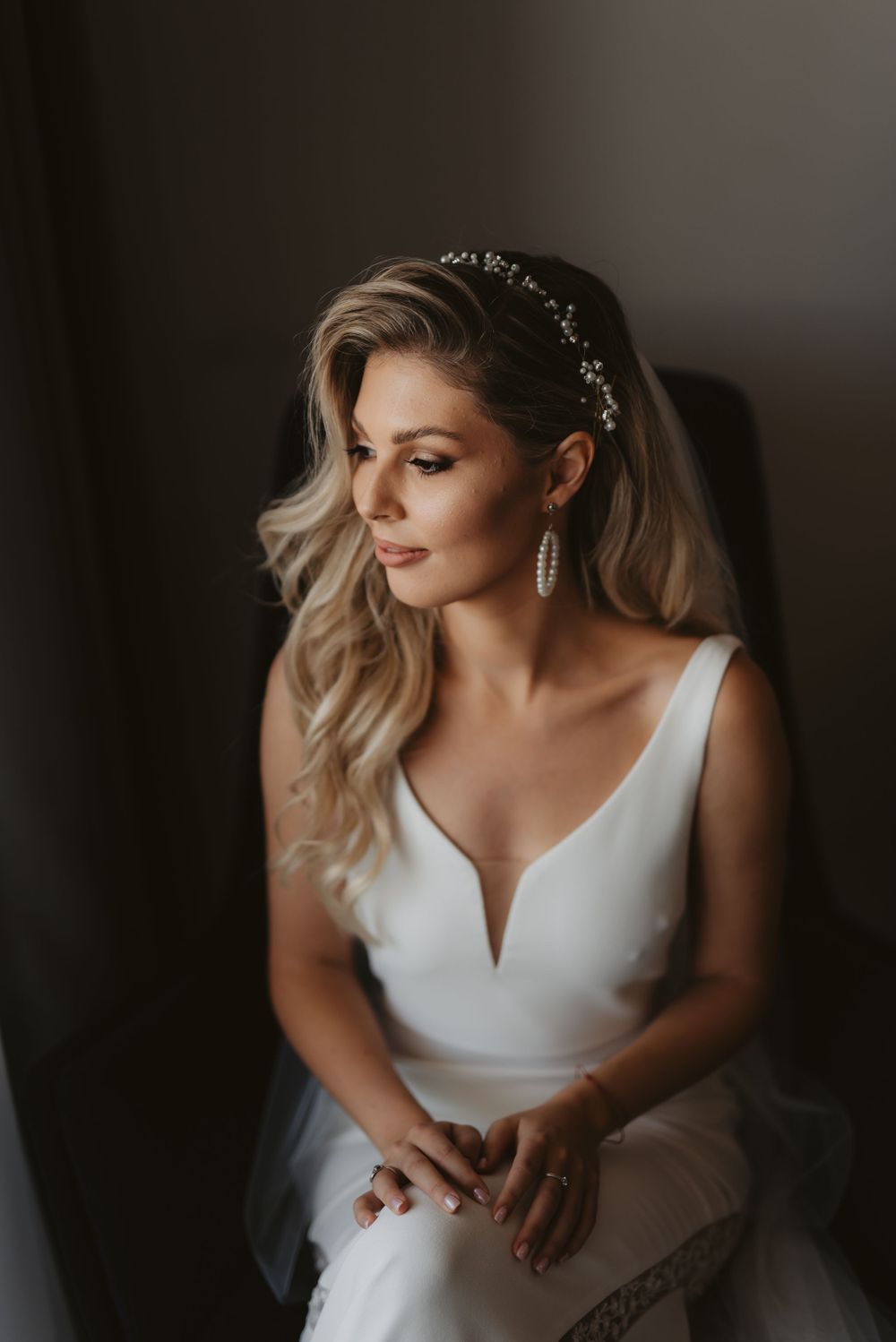 Elegant bridal portrait showcasing a plunging neckline wedding dress, crystal headpiece and styled blonde waves.