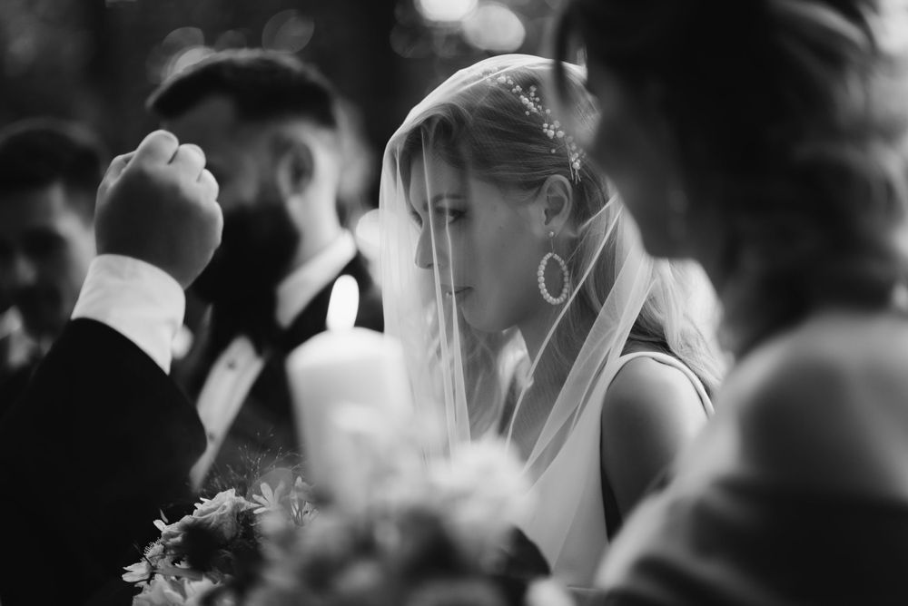 Black and white photo of bride wearing delicate veil during outdoor ceremony.