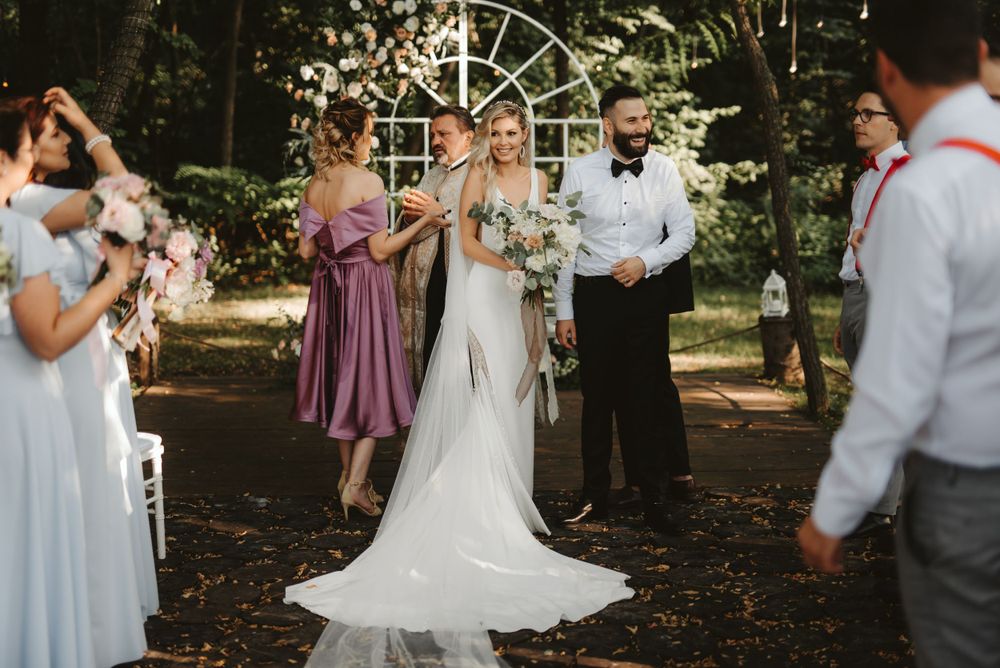 Wedding celebration under a decorative arch in a wooded outdoor setting.