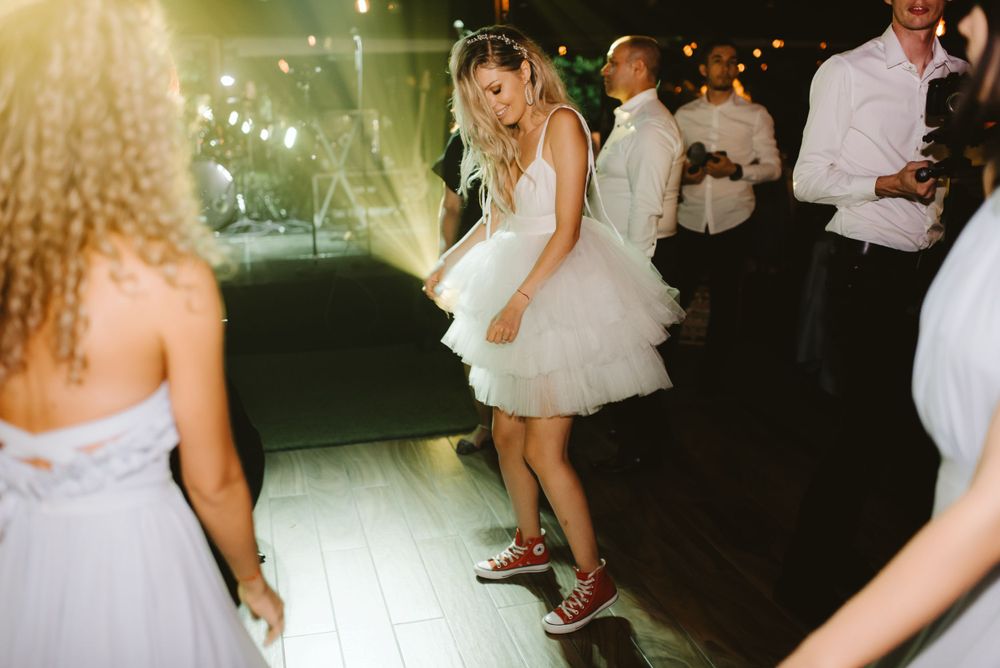 A person in a short white dress dances joyfully on an illuminated dance floor during a wedding reception.