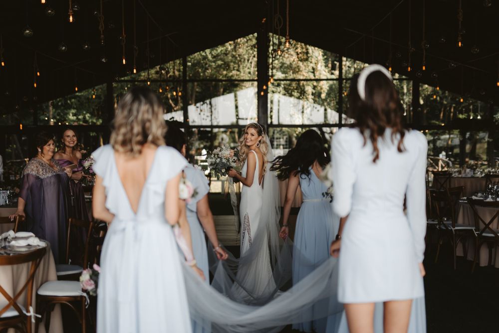 Wedding party in light colored dresses preparing in an elegant indoor venue with glass walls.