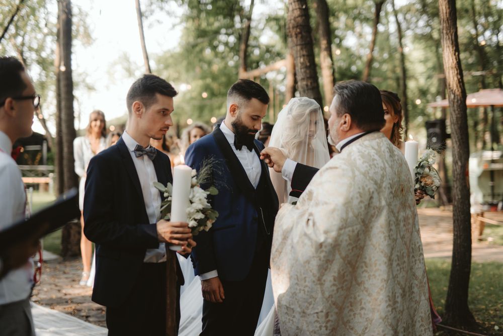 Outdoor wedding ceremony with wedding party in dark suits and officiant in white robes.