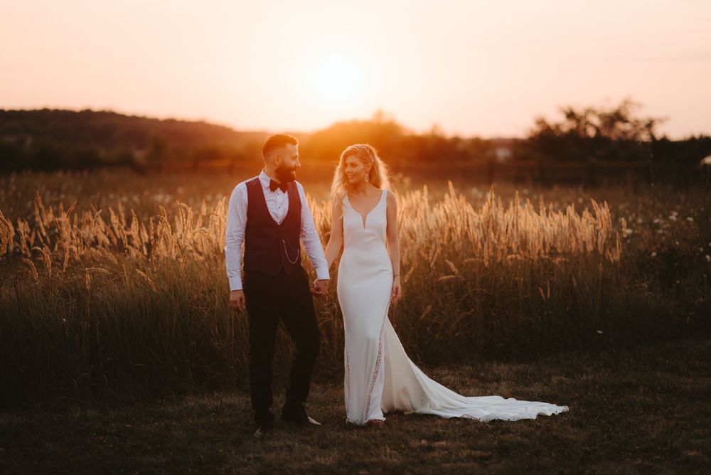 Bride and groom stand together in field during dramatic sunset.