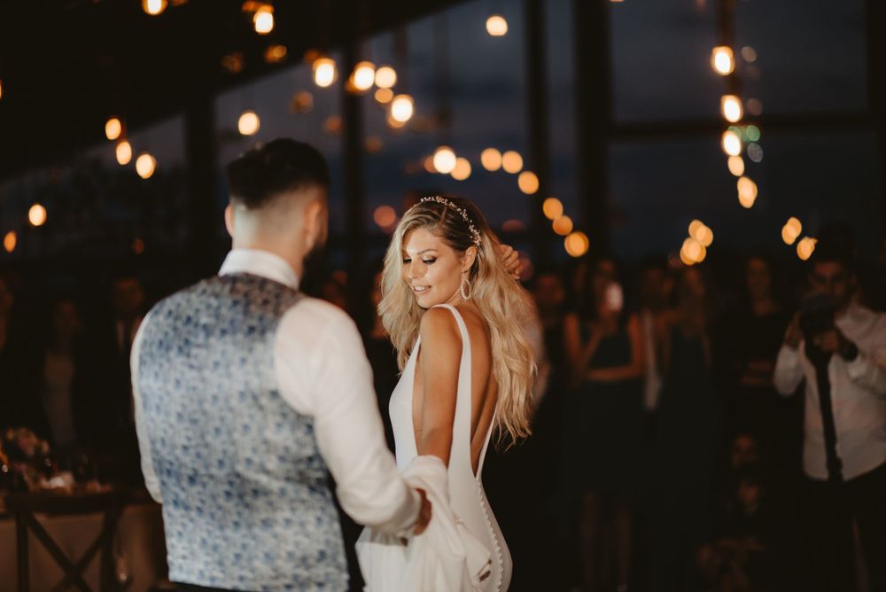 Couple dances at their reception under string lights with guests watching in background.