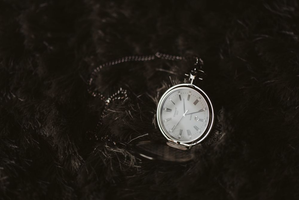 Vintage pocket watch with chain photographed on dark textured surface.