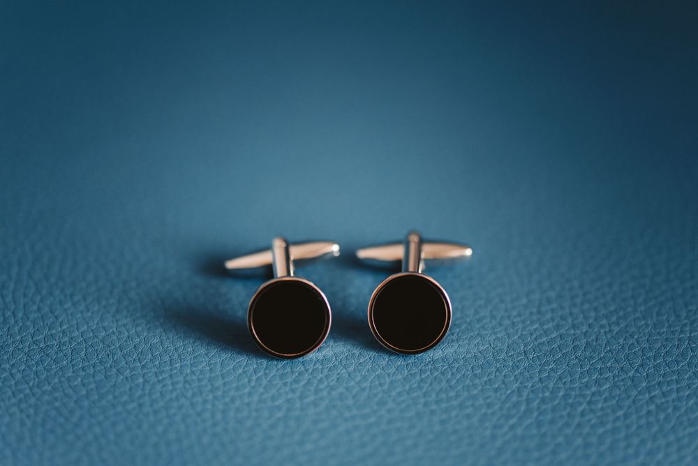 Round black cufflinks on textured blue leather background.
