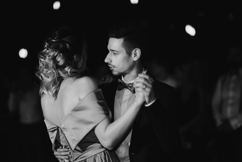 A couple dances intimately in a dimly lit ballroom with bokeh lights in the background.