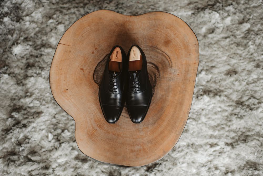Black formal dress shoes placed inside brown leather hat on carpet.
