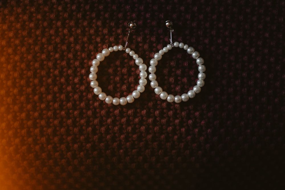 Pearl hoop earrings photographed on dark textured background with warm lighting.