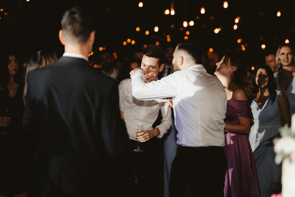 Wedding reception guests dancing and celebrating in a dimly lit venue.