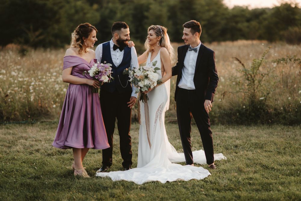 Wedding party of four poses together outdoors in formal attire.