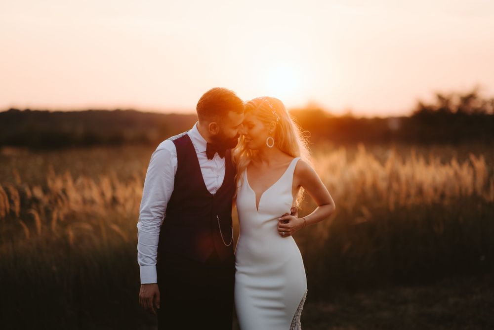 Couple shares romantic moment in backlit wheat field at dusk.