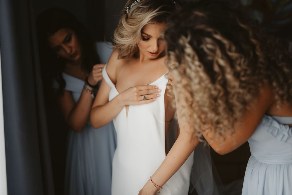 Bridesmaids in light blue dresses help bride get ready on wedding day.