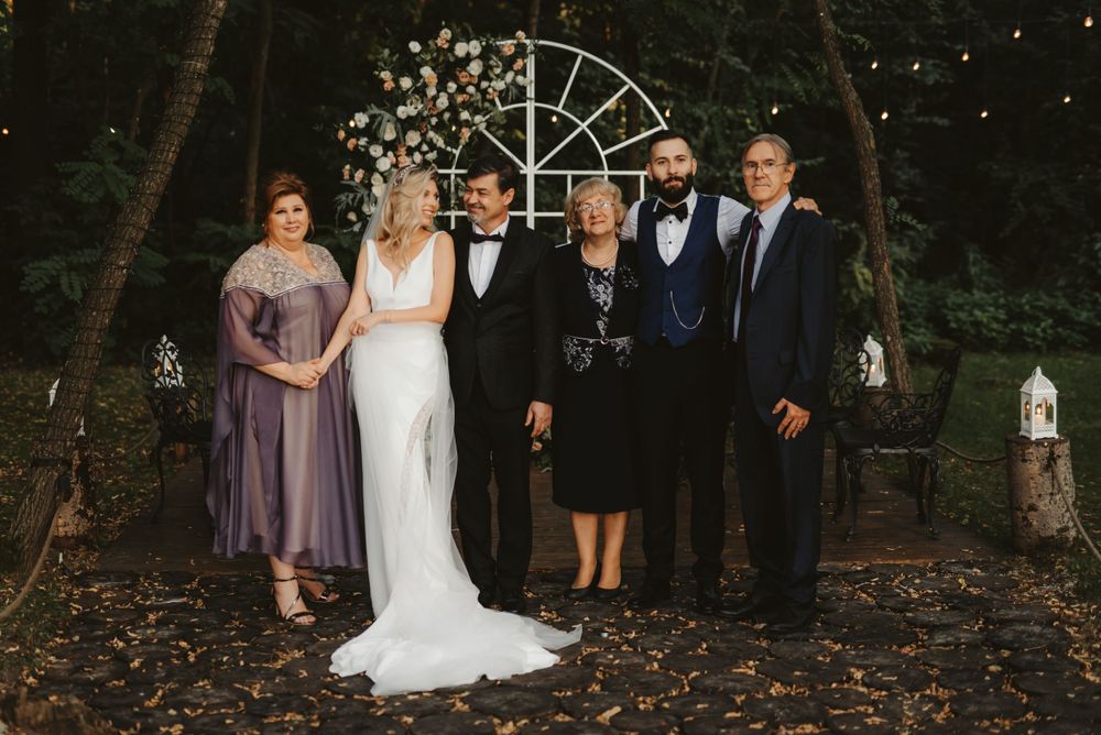Formal wedding party portrait under garden arch in wooded setting.