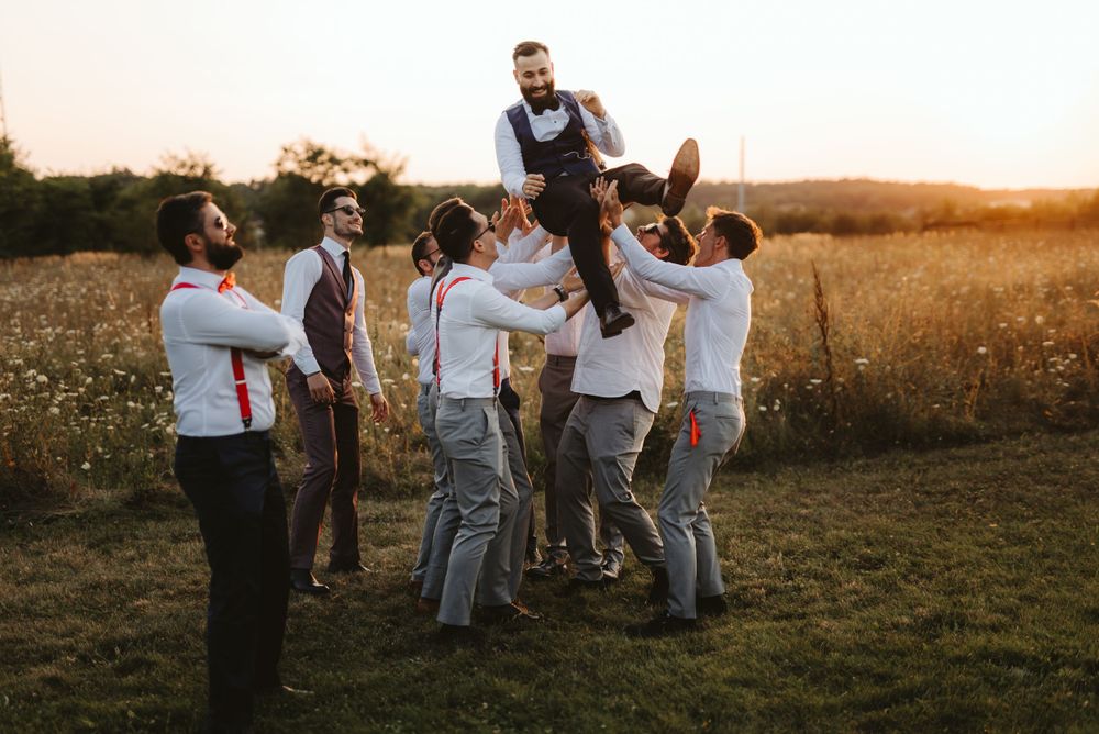 Groomsmen lift and celebrate during outdoor wedding photo session at sunset.