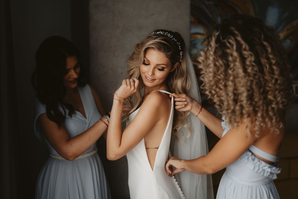 Candid moment of wedding preparation with bridesmaids assisting the bride.