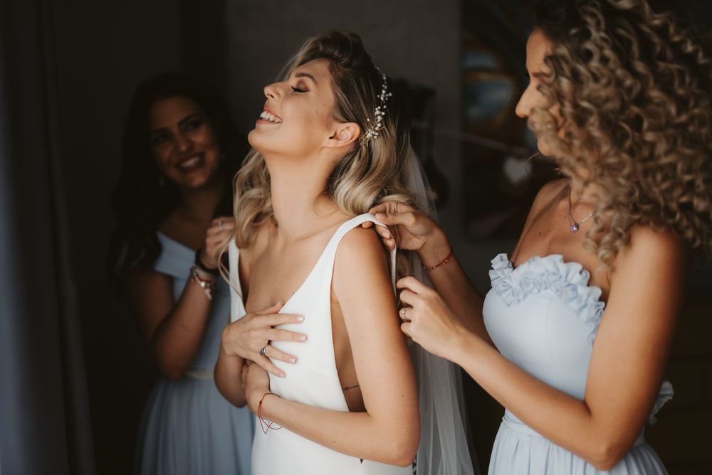 Wedding preparations with bridesmaids helping adjust the bride's elegant white gown.