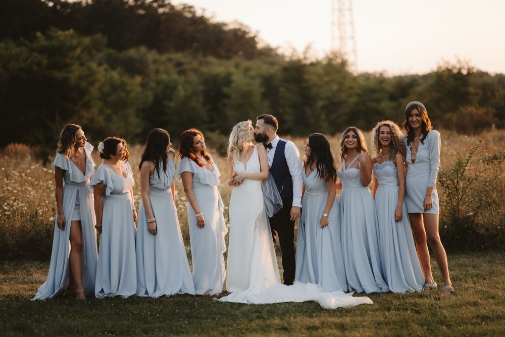 Wedding party in light blue dresses posed together during golden hour.
