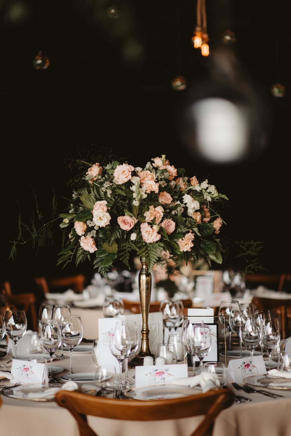 Romantic reception table with tall pink floral arrangement and hanging glass orb decorations.