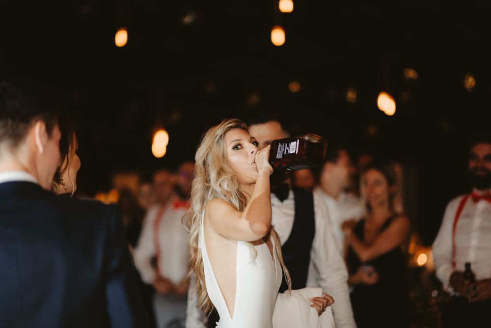 Bride takes a drink from a bottle during wedding reception celebrations.