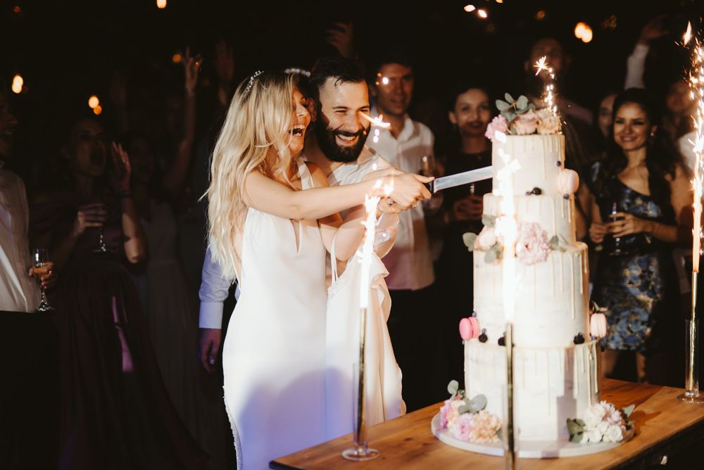 Wedding couple cutting their elegant white tiered cake during reception celebration.