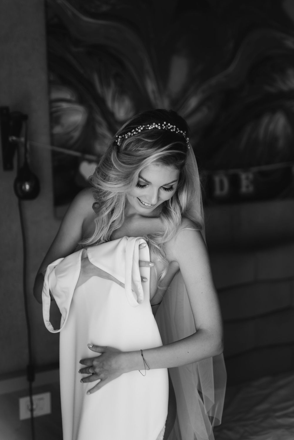 Black and white portrait of bride embracing her wedding dress in moody lighting.
