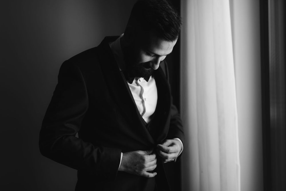 Dramatic black and white portrait of person adjusting bowtie in window light.