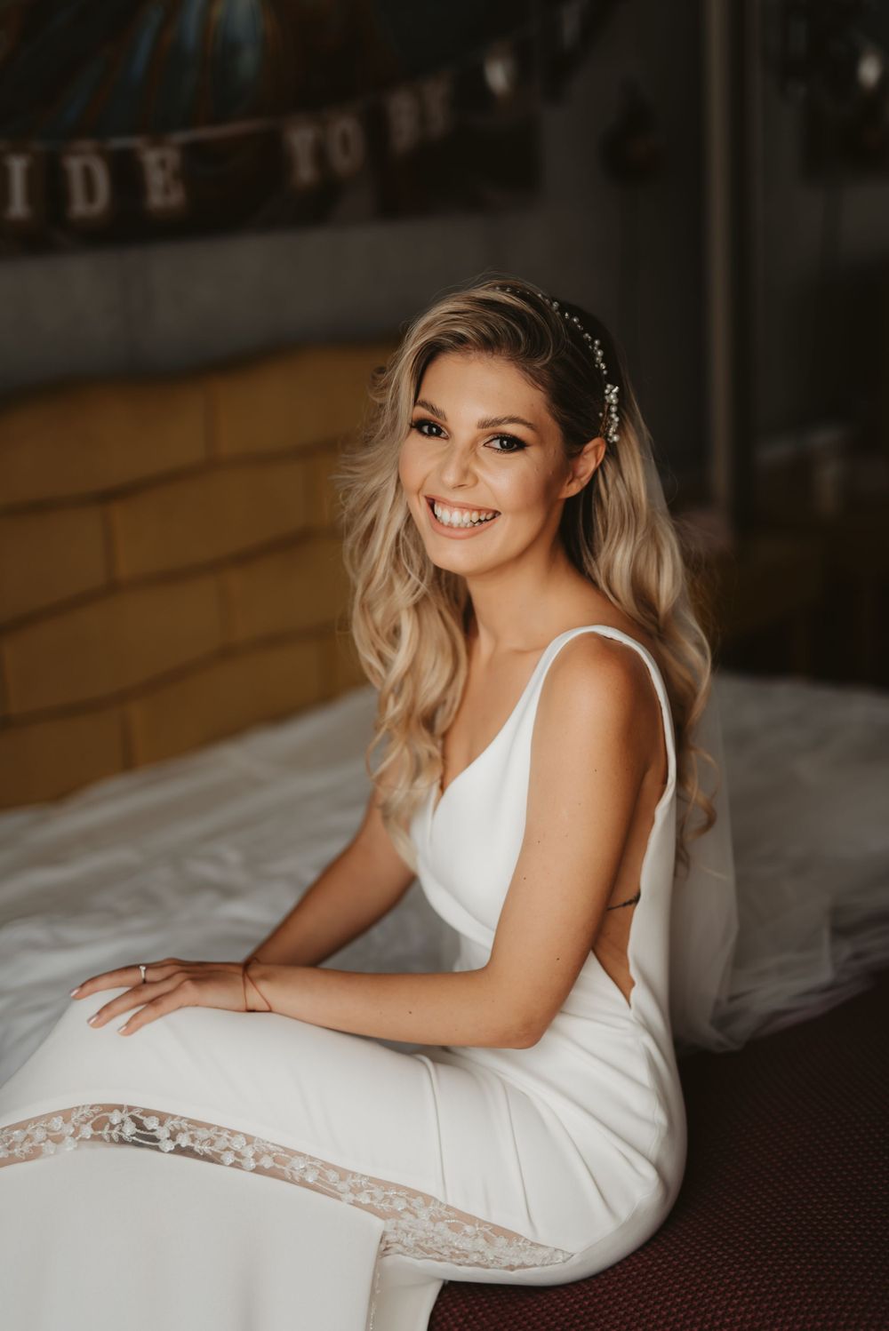 Elegant bride in fitted white gown sits while showing radiant smile.