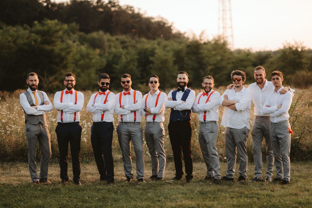 Wedding party groomsmen in matching suspenders and white shirts pose together outdoors.