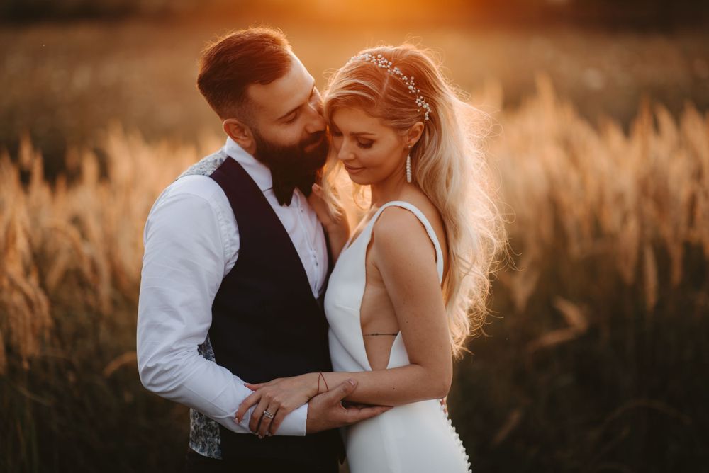 Intimate wedding portrait captured during golden hour in rustic field setting.