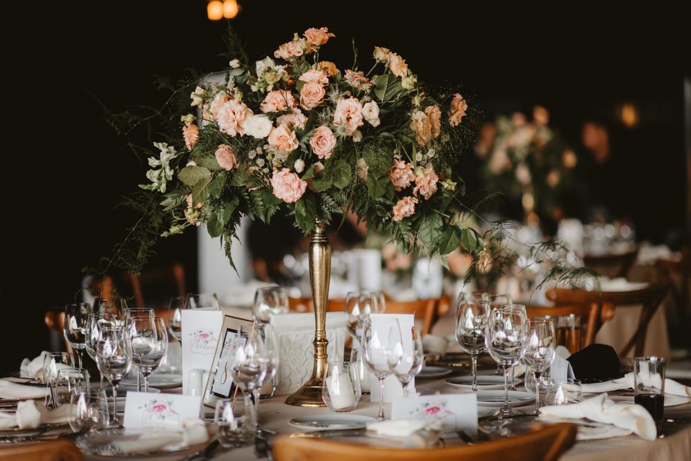 Elegant table setting with tall pink floral centerpiece and multiple wine glasses.