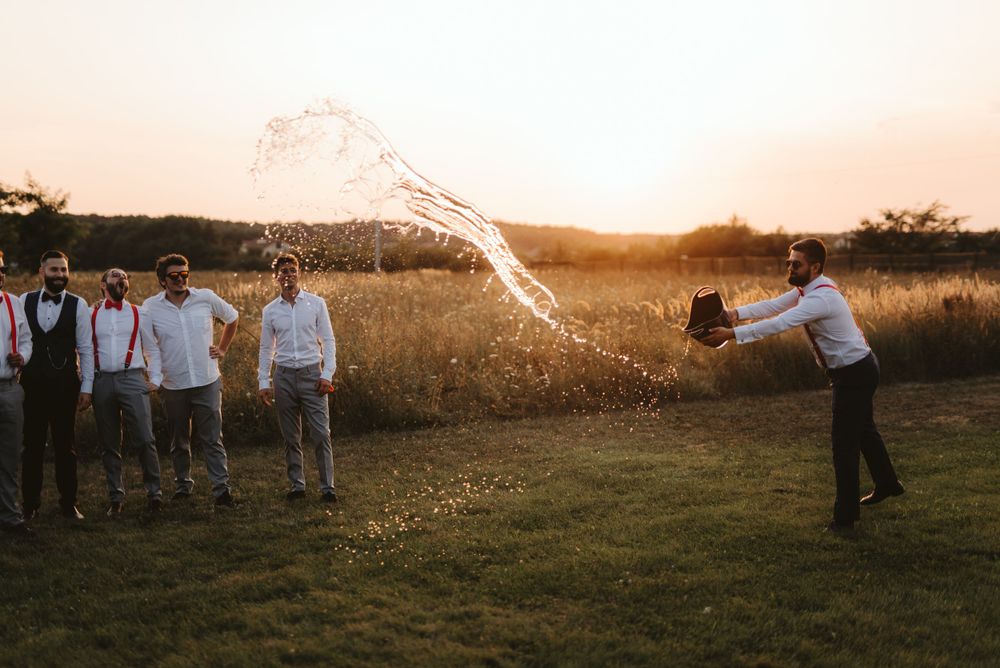 Groomsmen spray champagne during outdoor wedding celebration at golden hour.