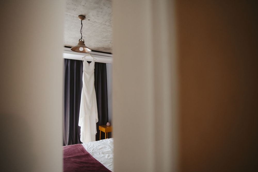 White wedding dress hanging in window with dark curtains and ceiling fan.
