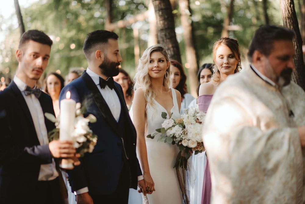 Wedding party stands together outdoors among trees with bridesmaids in purple dresses.