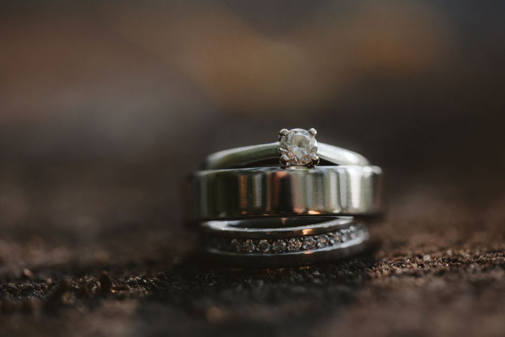 Close-up of diamond engagement ring and wedding band on textured dark surface.