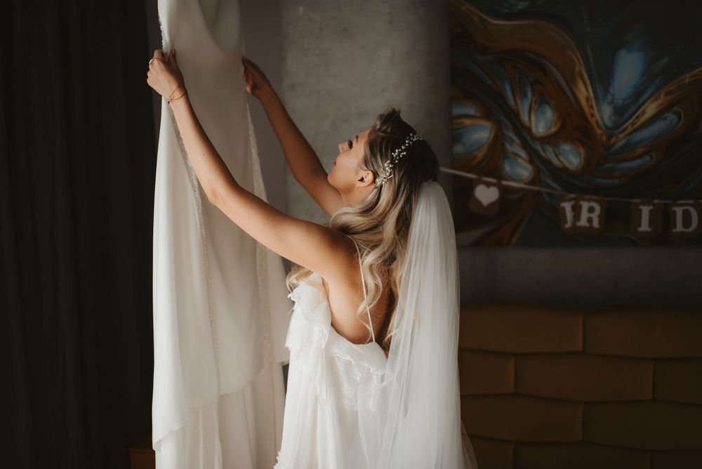Side view of someone in white dress reaching up to adjust curtains.