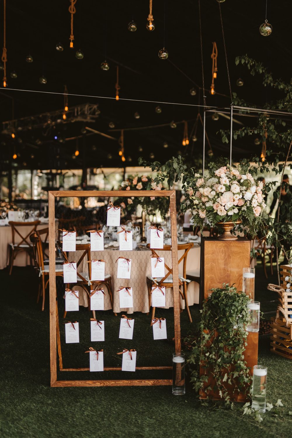 Rustic wooden seating chart display with hanging cards and floral decorations at wedding venue.