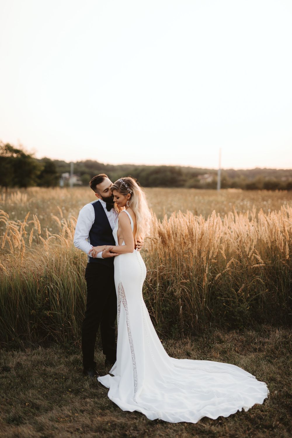 Wedding couple embraces in tall grass field during golden hour.
