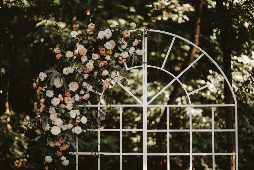 White garden arch trellis decorated with delicate pink and white flowers in a natural outdoor setting.