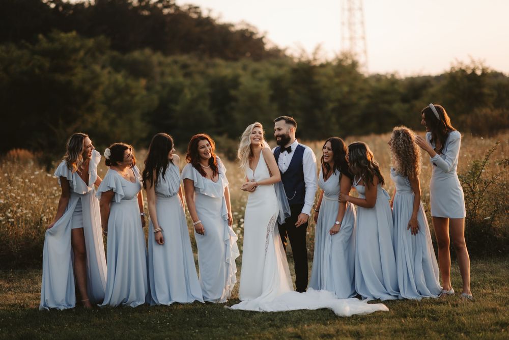 Bridal party in flowing blue gowns laughing together at sunset.