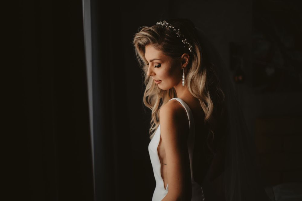 Side profile of bride in sleek white dress with delicate tiara and flowing blonde hair.