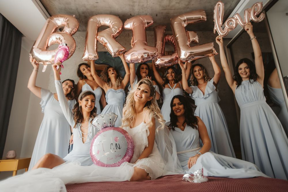 Group celebration with rose gold 'BRIDE' balloons and light blue dresses.