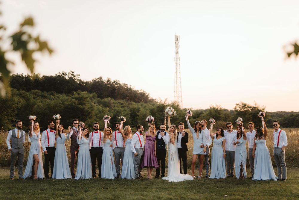 Full wedding party poses together outdoors in coordinated attire at sunset.