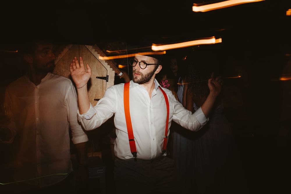 Party guest in suspenders dancing energetically in a dimly lit reception space with motion blur effects.