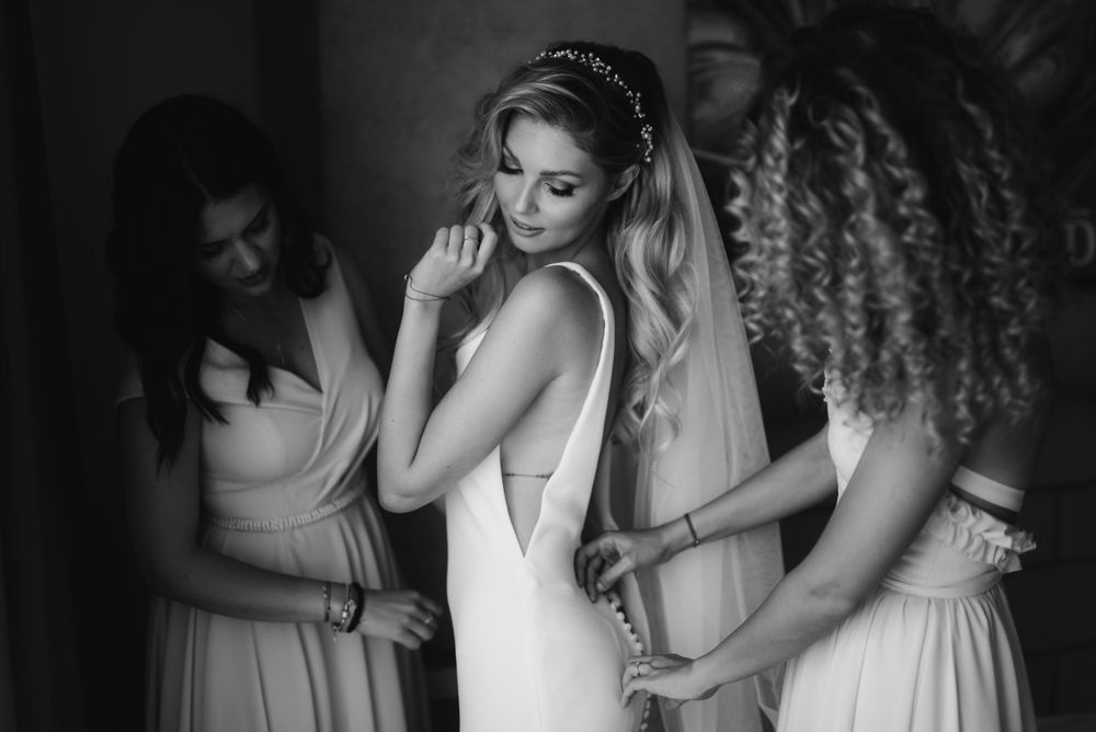 Monochrome capture of bridal preparations with attendants helping with final touches.
