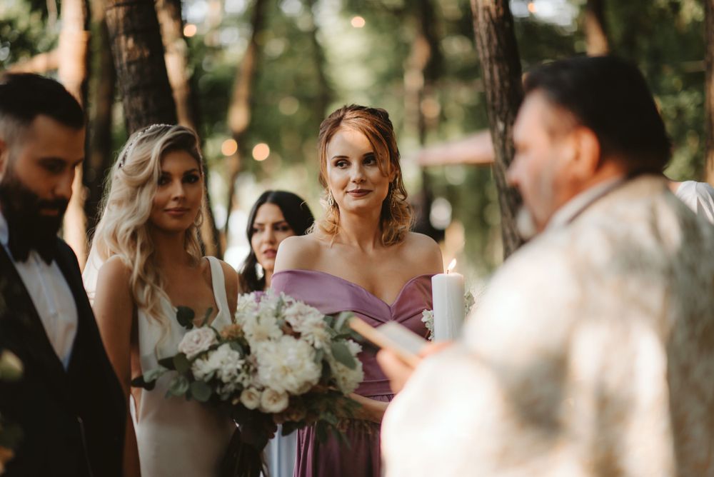 Wedding ceremony in progress among trees with bridal party holding white floral bouquets.