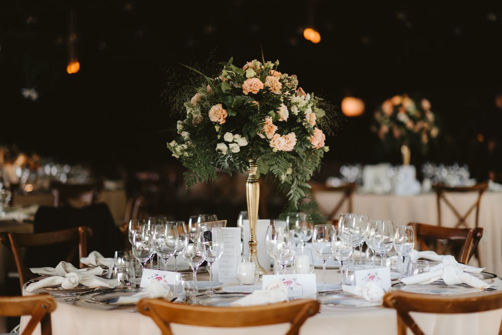 Elegant wedding table setting with tall floral centerpiece and wine glasses in romantic indoor venue.