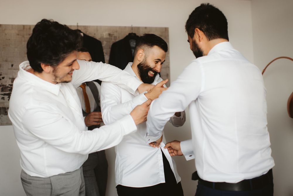 Friends helping adjust formal attire during wedding preparations.