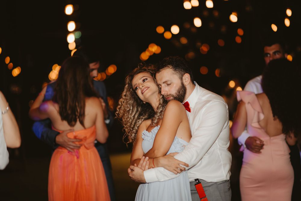 Couples slow dance under romantic lighting at an evening celebration.